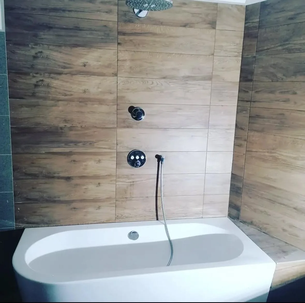 Badewanne in Wien mit großformatigen Holzoptik-Fliesen an der Wand, Unterputz-Thermostat, Regenduschkopf und Handbrause — natürliche Wellness-Atmosphäre (Referenz 2F Installation OG)