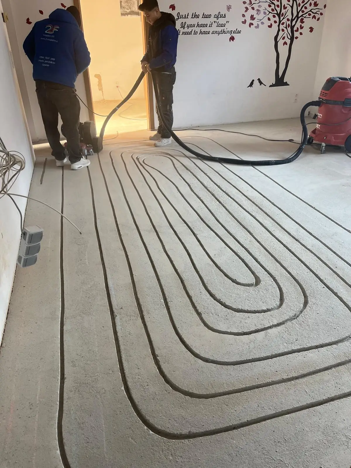 Fußbodenheizung fräsen Wien — 2F-Installateure am Werk: Diamantfräse schneidet millimetergenau Kanäle in den vorhandenen Estrich, Direktabsaugung verhindert Staub im Wohnraum (nachträgliche Installation im Altbau)