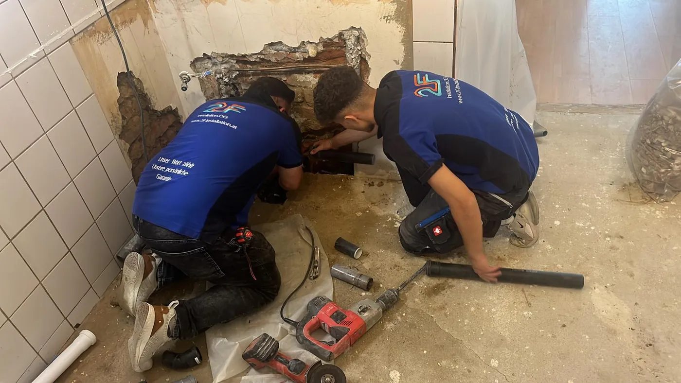 Rohrbruch-Reparatur Wien — zwei Monteure der 2F Installation OG legen ein beschädigtes Abflussrohr im Mauerwerk frei und tauschen das Rohrstück (Leitungsschaden-Notdienst, 1180 Wien)