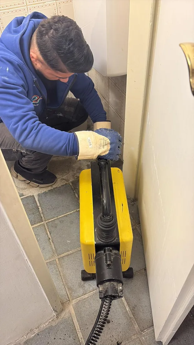 Rohrreinigung Wien — Monteur der 2F Installation OG beseitigt eine WC-Verstopfung mit elektromechanischer Rohrreinigungsmaschine (Spirale) im Badezimmer (24h Abfluss-Notdienst)